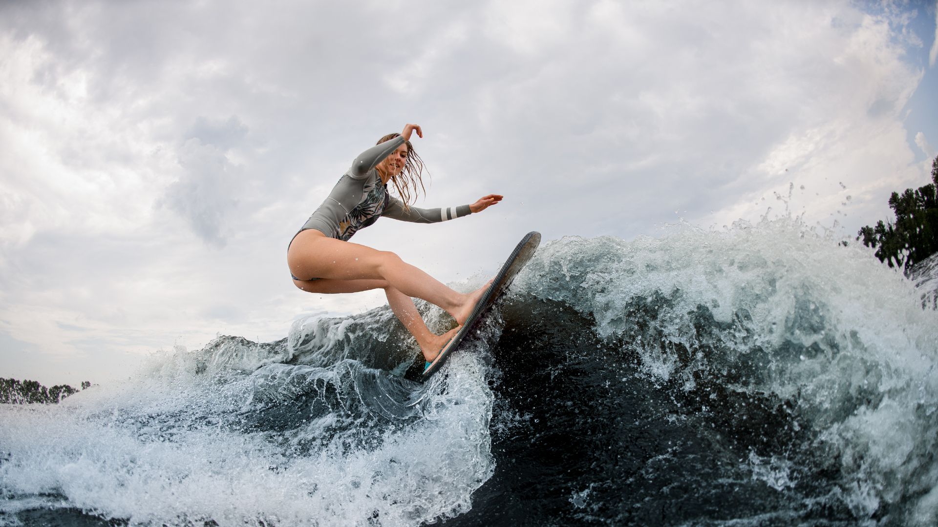 A person in a long-sleeve rash guard and swimsuit rides a wave on a surfboard under a cloudy sky—one of the top Tamarindo activities and an essential experience for those seeking things to do in Tamarindo Costa Rica.
